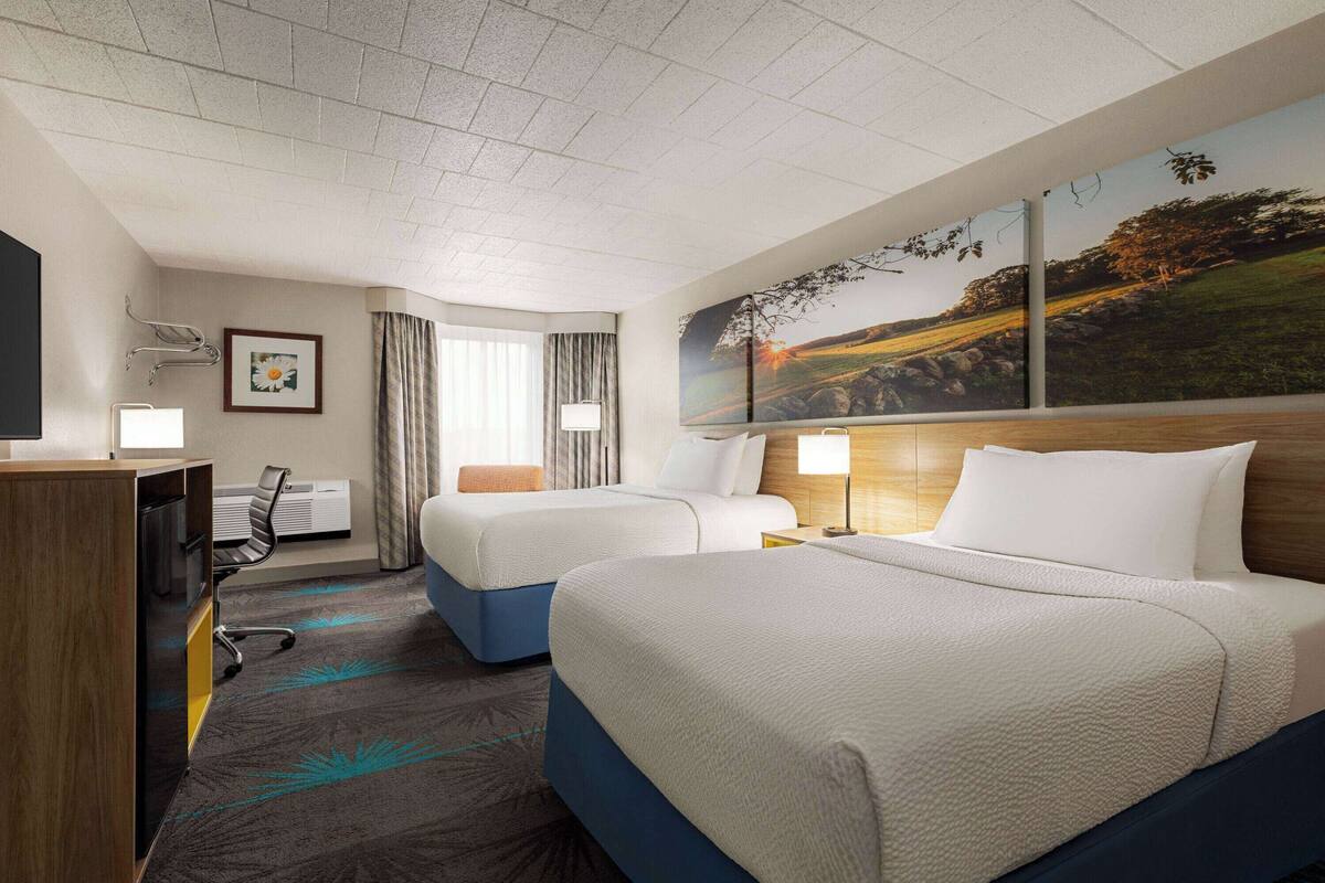 Ein Hotelzimmer mit zwei Betten, einem Schreibtisch, einem Stuhl, einem Fernseher und einem Bild an der Wand.
