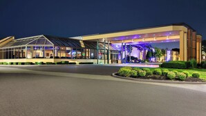Un hotel moderno con fachada de vidrio, entrada cubierta y jardines bien cuidados.