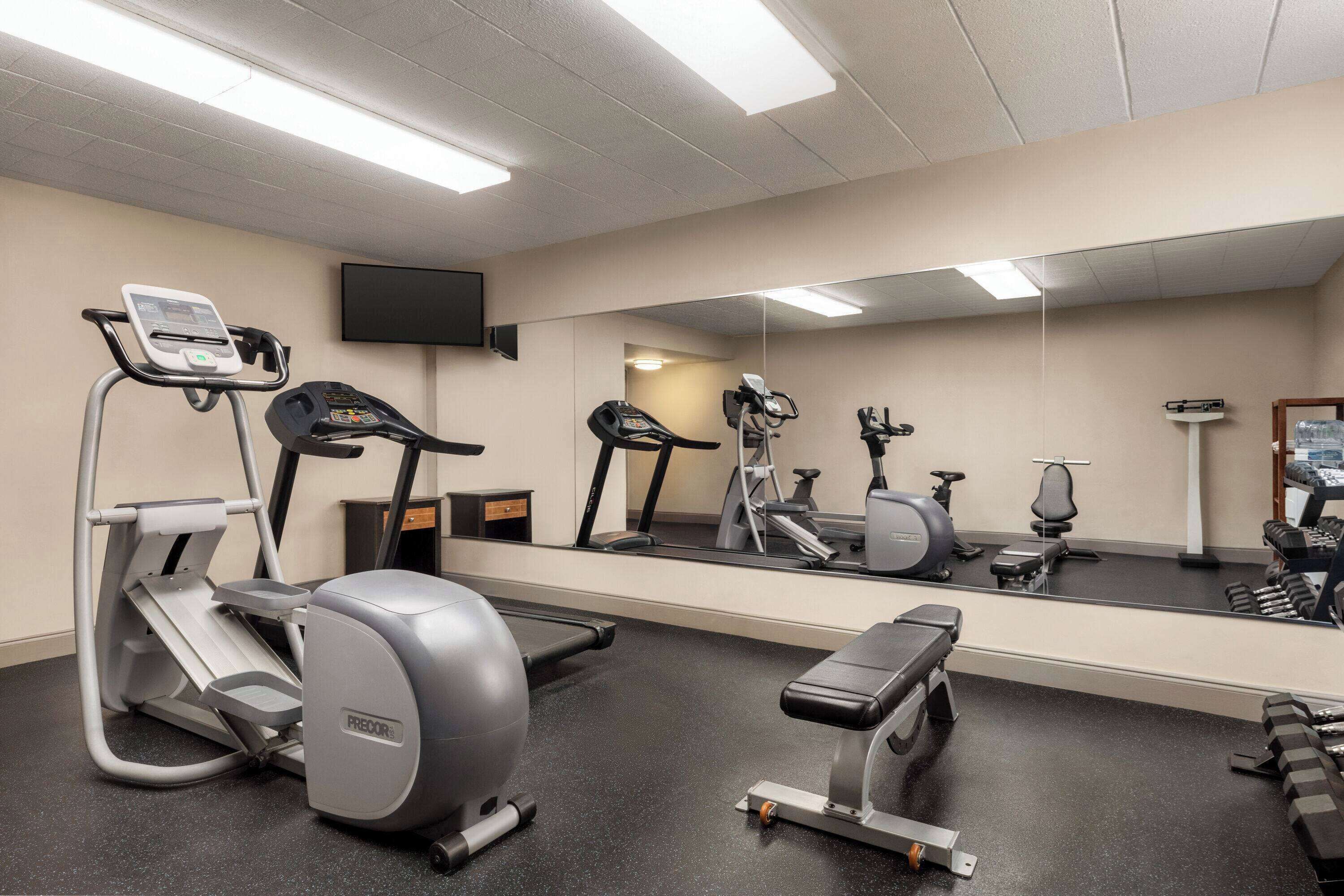 A gym with cardio equipment, weights, and a mirror.