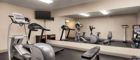 A gym with cardio equipment, weights, and a mirror.