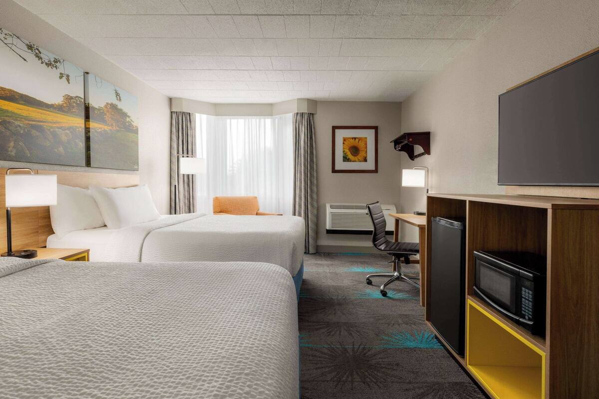 Ein Hotelzimmer mit zwei Betten, einem Schreibtisch, einem Stuhl, einem Fernseher und einer Mikrowelle.