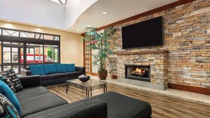 Una sala de estar moderna con chimenea de piedra, televisor de pantalla plana y un ventanal con vista a un estacionamiento.