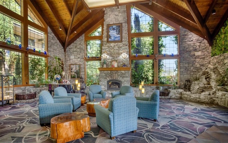 A spacious lobby with high ceilings, stone walls, and large windows. There are several seating areas with blue upholstered chairs and a fireplace.