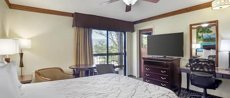 A hotel room with a large bed, a desk with a computer, a television, and a ceiling fan.