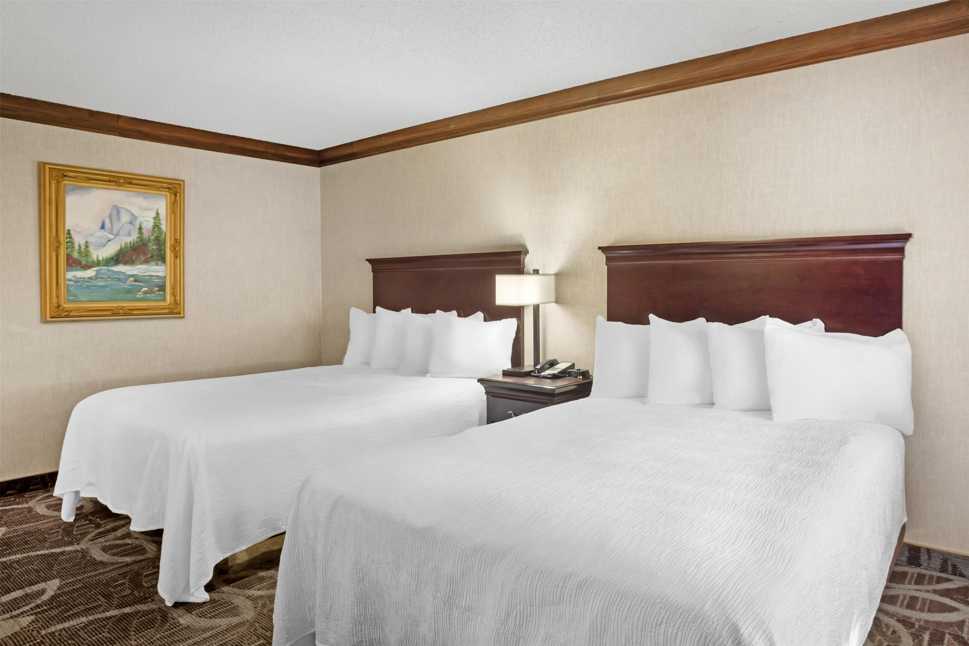A hotel room with two beds, a painting on the wall, and a nightstand with a lamp.
