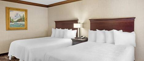A hotel room with two beds, a painting on the wall, and a nightstand with a lamp.