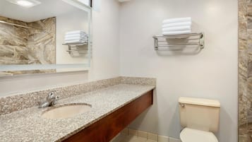 A bathroom with a granite countertop sink, a mirror, a toilet, and towel racks on the wall.