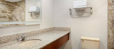 A bathroom with a granite countertop sink, a mirror, a toilet, and towel racks on the wall.