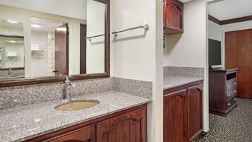 A bathroom with a granite countertop sink, wooden cabinets, a mirror, and a towel rack.