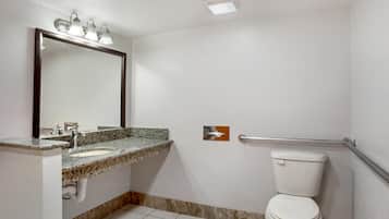 Un baño con lavamanos de encimera de granito, un espejo grande, un inodoro blanco y un pasamanos.