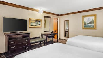 Habitación de hotel con dos camas, un escritorio, una silla, televisión y obras de arte en las paredes.
