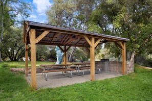 A wooden pavilion with picnic tables and a statue in a park.