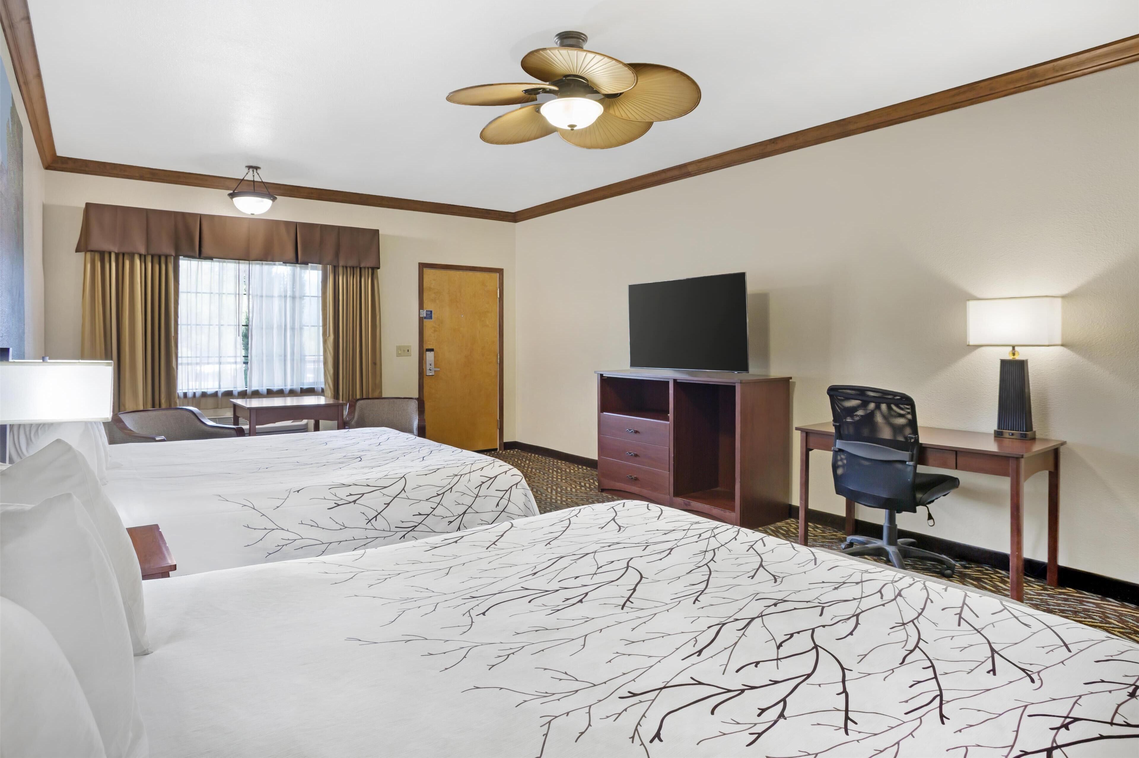 Een hotelkamer met twee bedden, een bureau, een stoel, een televisie en een plafondventilator.