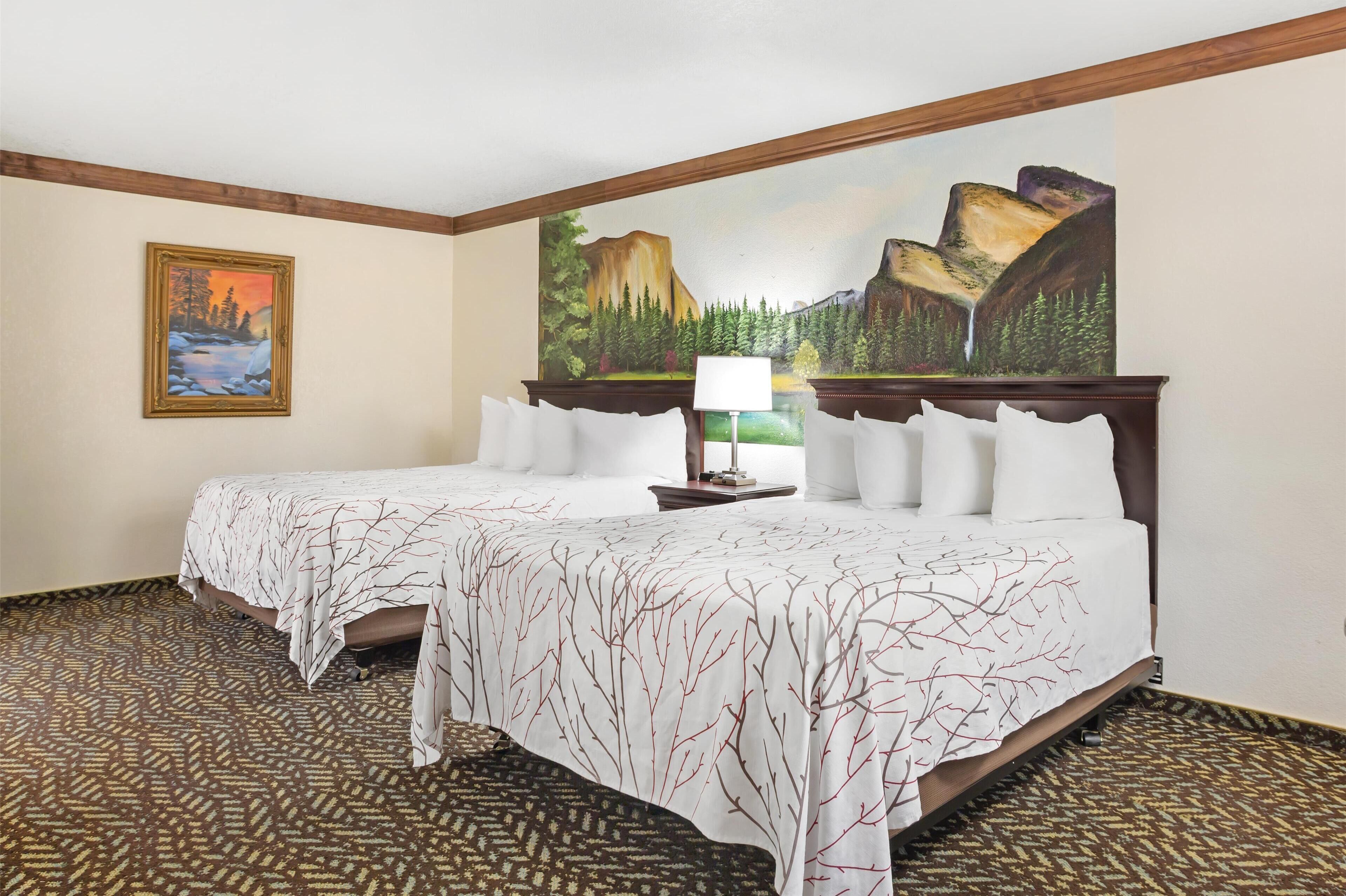 A hotel room with two beds, a painting of a mountainous landscape, a patterned carpet, and a wooden headboard.
