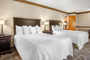 A hotel room with two beds, each with a wooden headboard, white bedding, and bedside lamps.