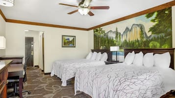 A hotel room with two beds, a desk, a chair, a ceiling fan, and a painting of a forest on the wall.