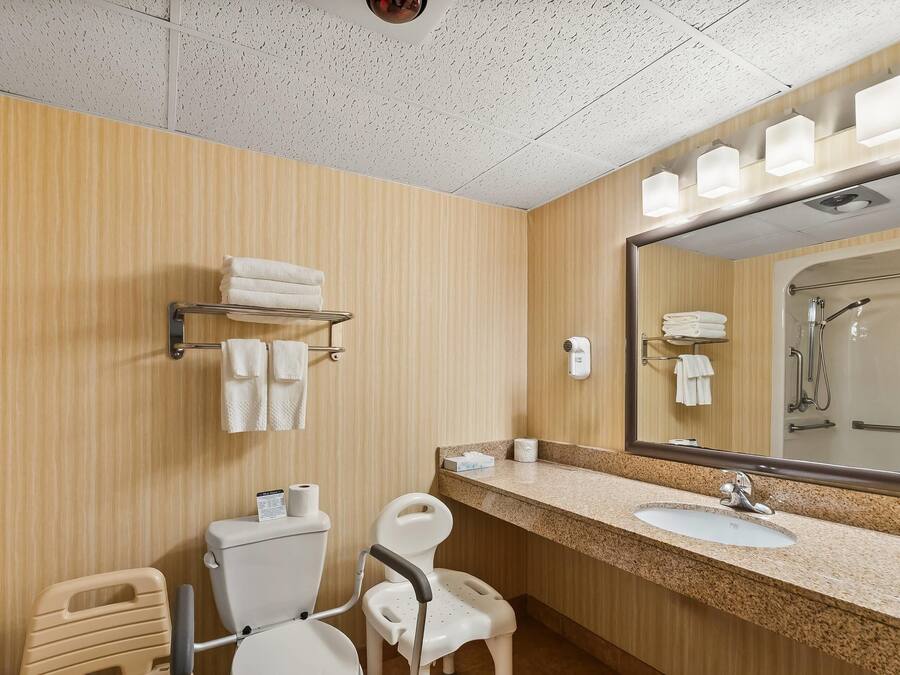 A modern bathroom with a wooden wall, a sink with a mirror, and a toilet.