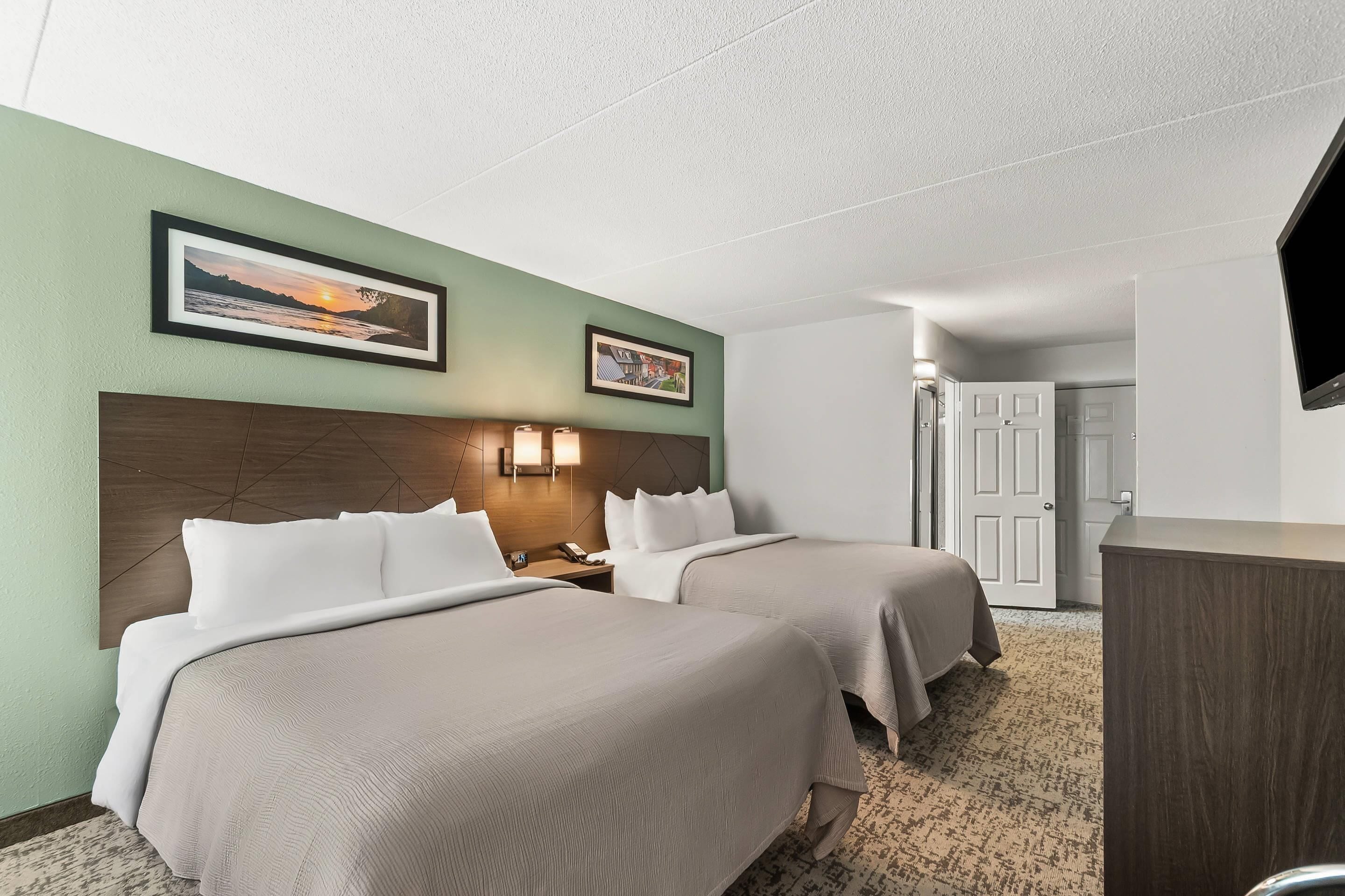 A hotel room with two beds, a wooden headboard, a desk, a television, and framed pictures on the wall.
