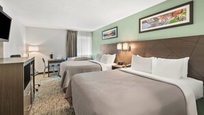 A hotel room with two beds, a desk, a chair, a TV, and a painting on the wall.