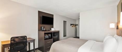 Una habitación de hotel con cama, escritorio, silla, televisión y una pequeña kitchenette.