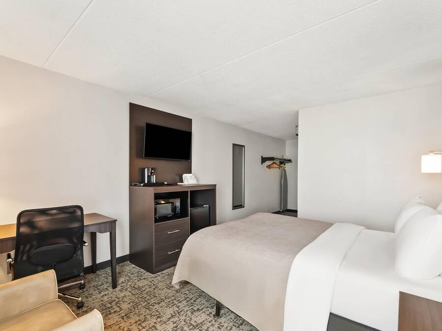 A hotel room with a bed, a desk, a chair, a TV, and a small kitchenette.