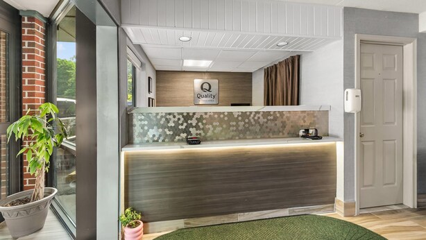 A hotel reception area with a modern design, including a reception desk, a sign that reads "Quality by Choice Hotels," and a potted plant.