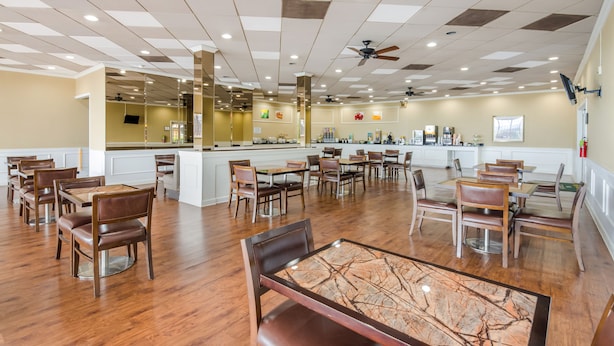 Un grand espace dédié à la salle à manger, avec plusieurs tables et chaises, un îlot central doté d’un comptoir et un ventilateur de plafond.