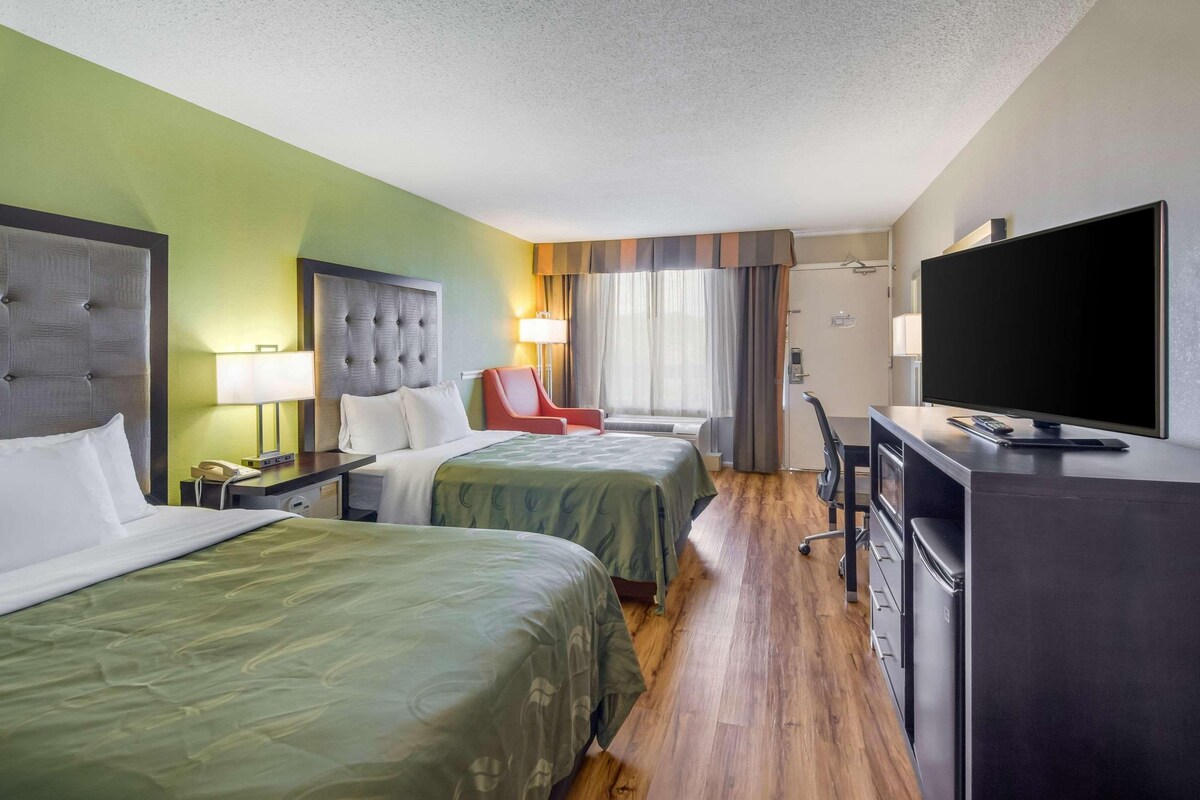 A hotel room with two beds, a desk, a TV, and a chair.