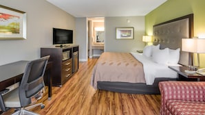 Une chambre d’hôtel avec un lit, un bureau, une chaise, une télévision et une salle de bain visible à travers une porte ouverte.