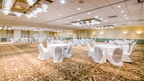 Une vaste salle de banquet avec des tables rondes recouvertes de nappes blanches et des chaises, une moquette à motifs et des lustres.