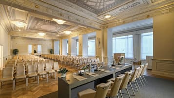 A conference room with rows of chairs, a long table with microphones, and a decorative ceiling.