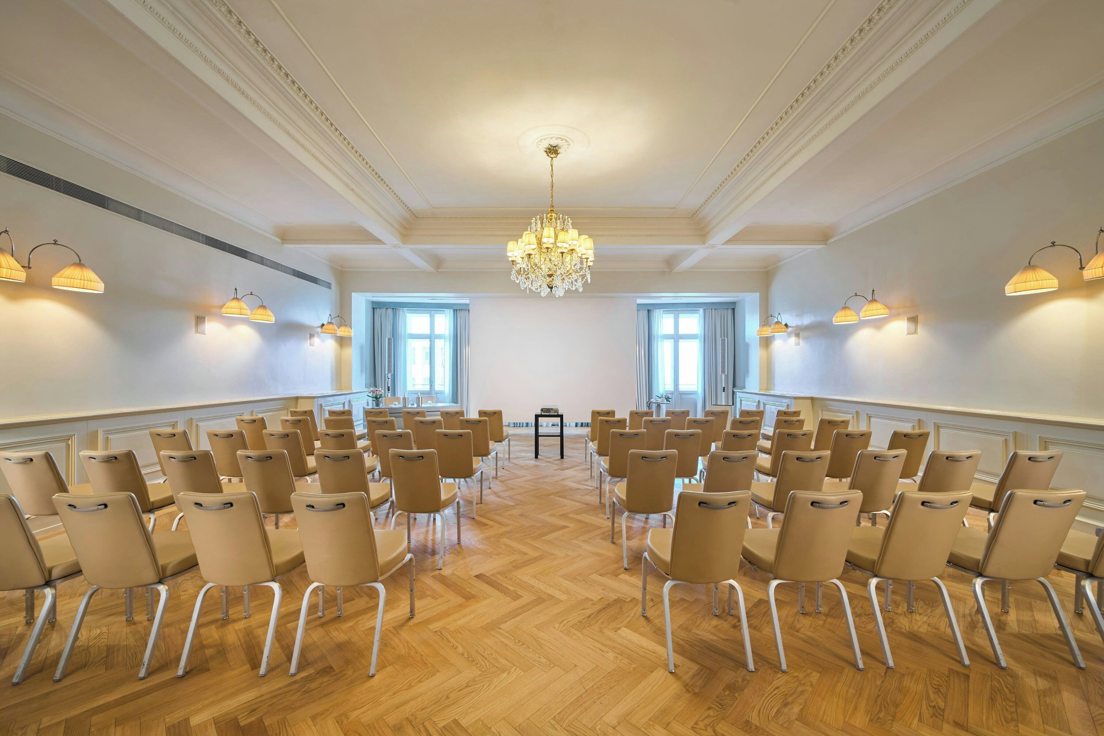 A conference room with rows of chairs, a chandelier, and large windows.