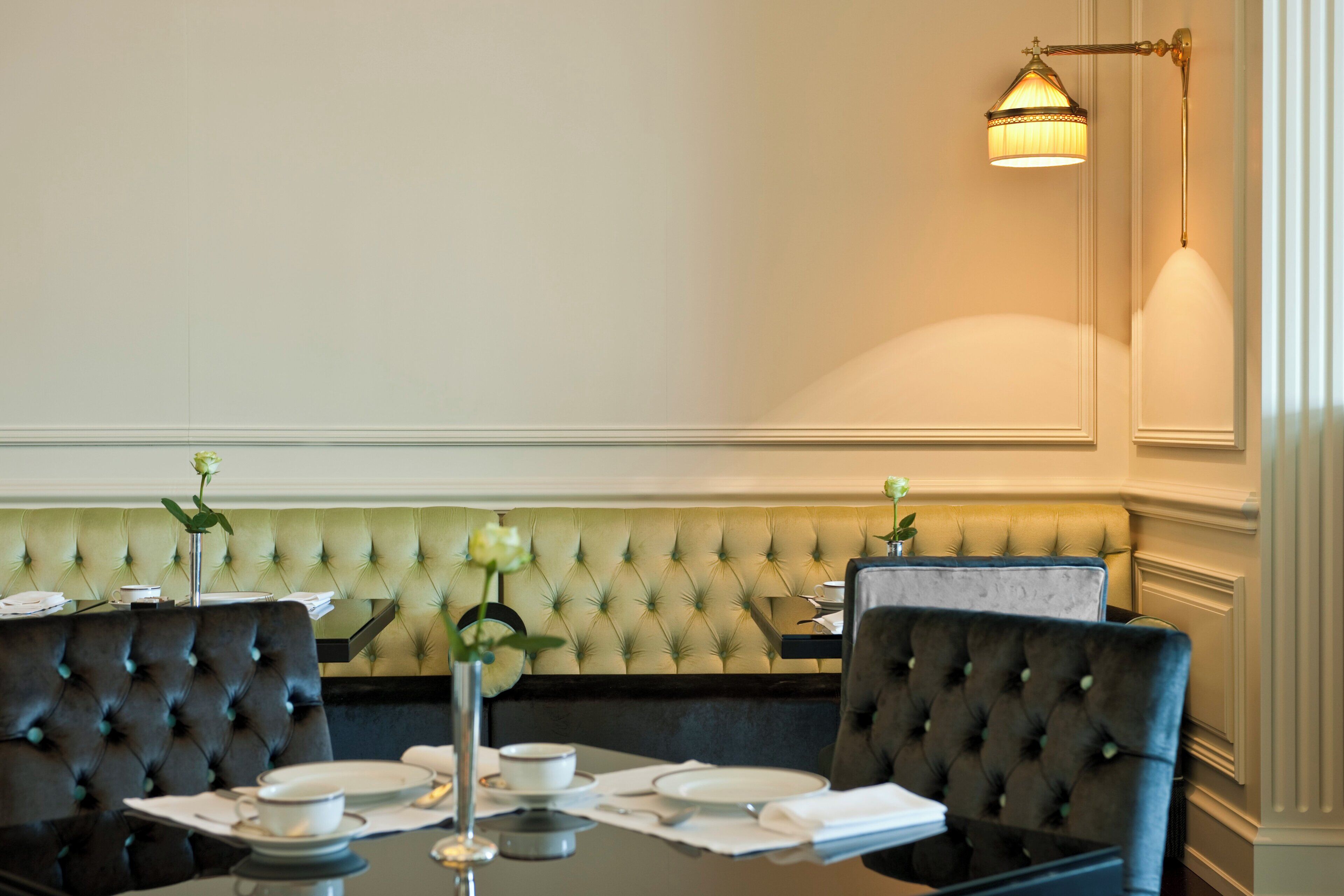 A dining area with a tufted green bench, black upholstered chairs, and a table set with plates, cups, and a vase with a flower.