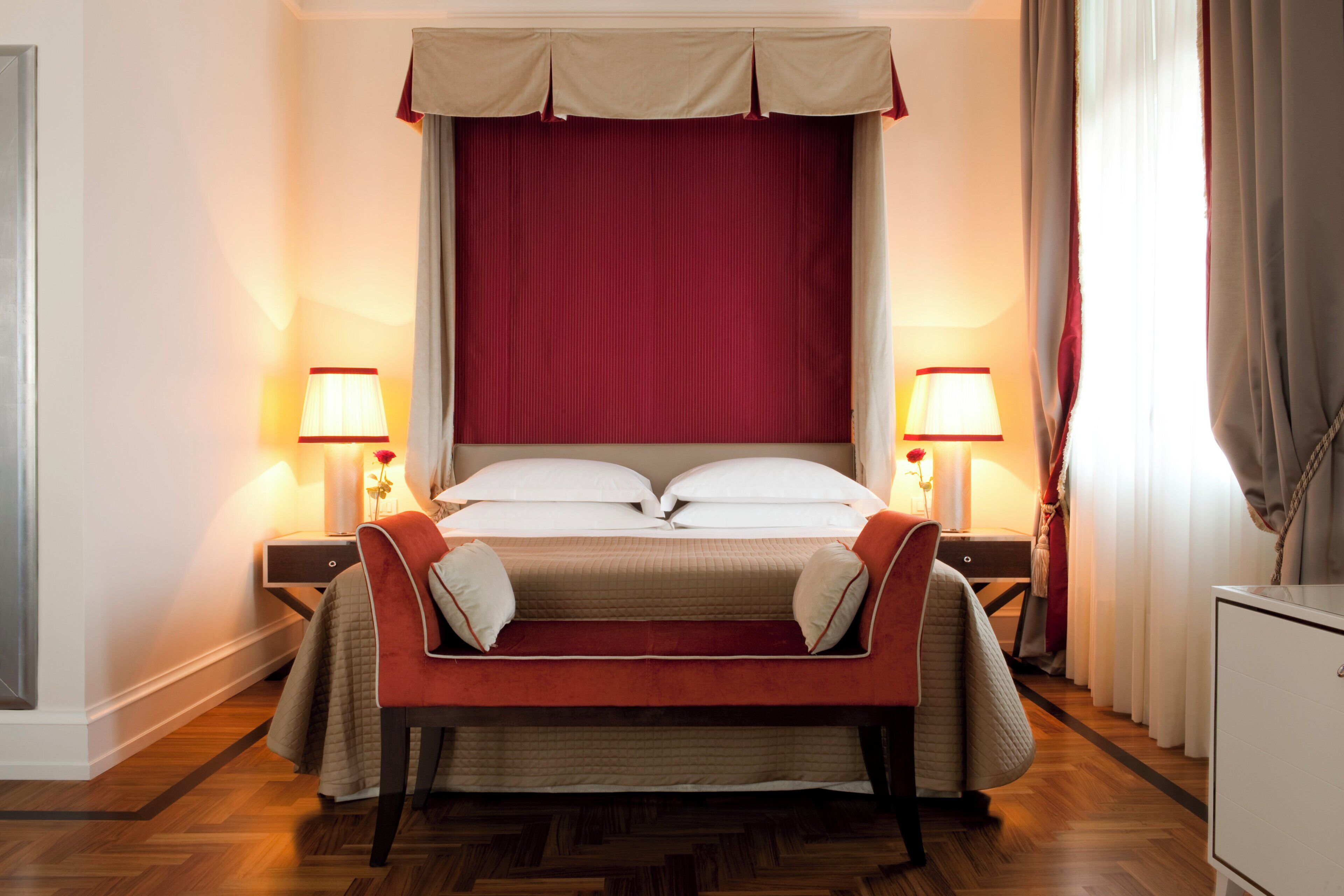 Ein Hotelzimmer mit einem großen Bett, zwei Nachttischlampen, einem roten Kopfteil, einem Sofa und einem kleinen weißen Schrank.