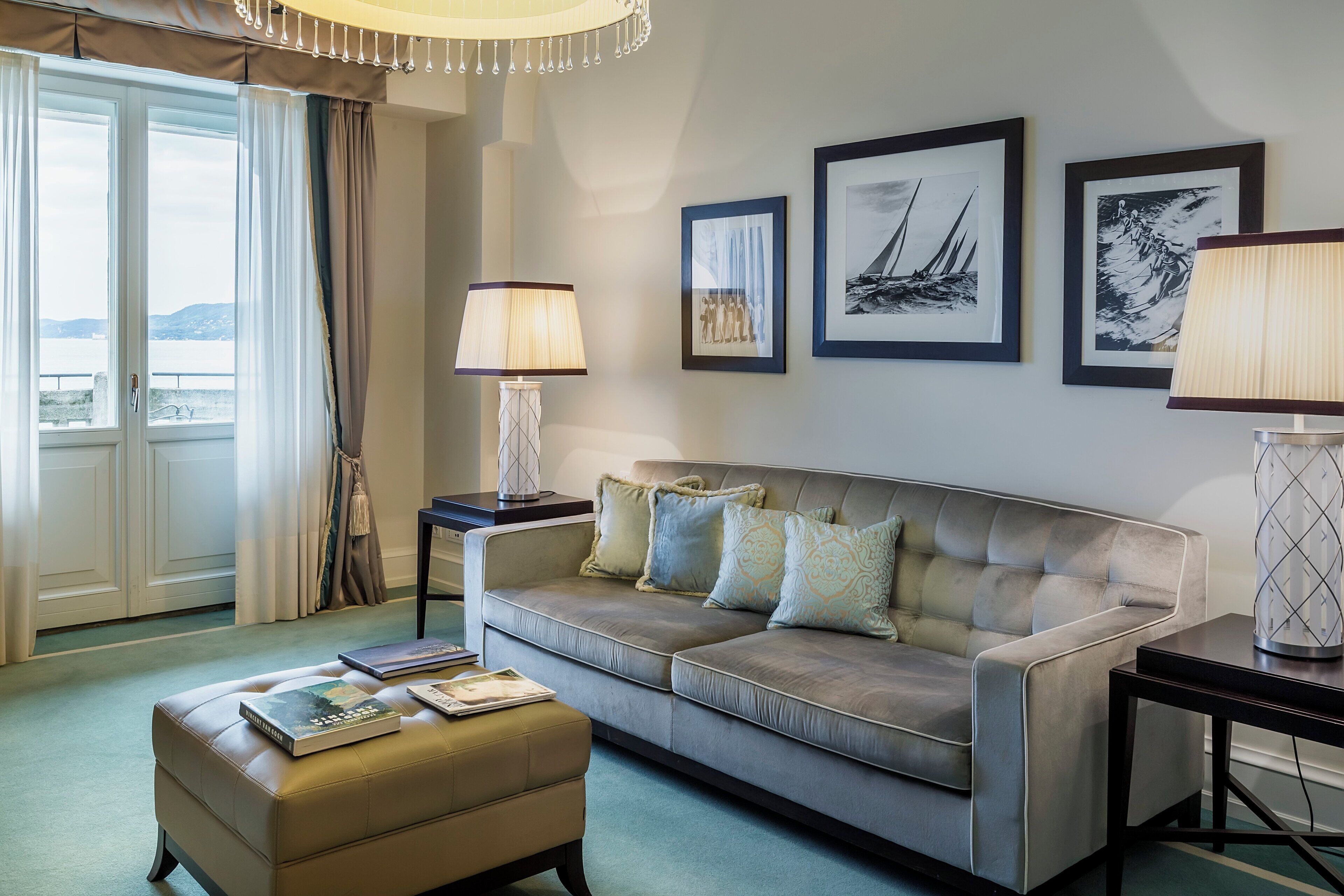 A hotel room with a sofa, ottoman, two side tables, a lamp, and framed artwork on the wall.