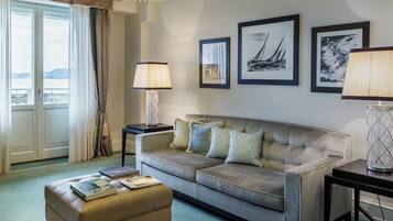 A hotel room with a sofa, ottoman, two side tables, a lamp, and framed artwork on the wall.