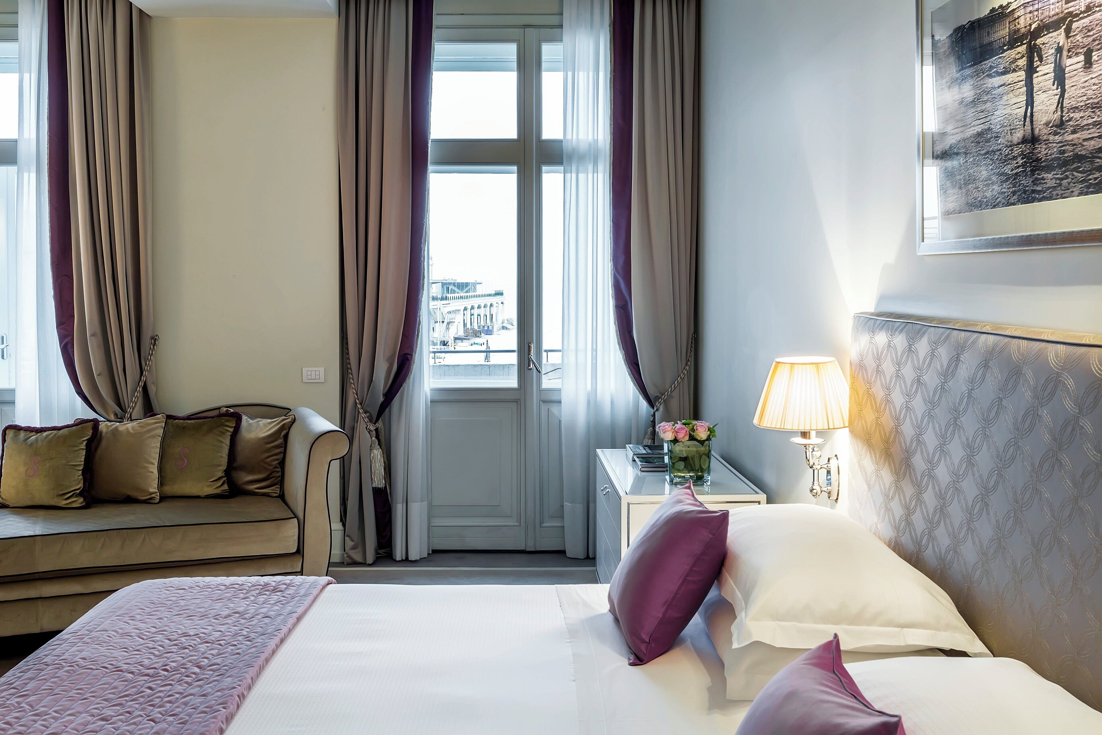 Ein Hotelzimmer mit Bett, Sofa, Nachttisch mit Lampe und einem Fenster mit Vorhängen.