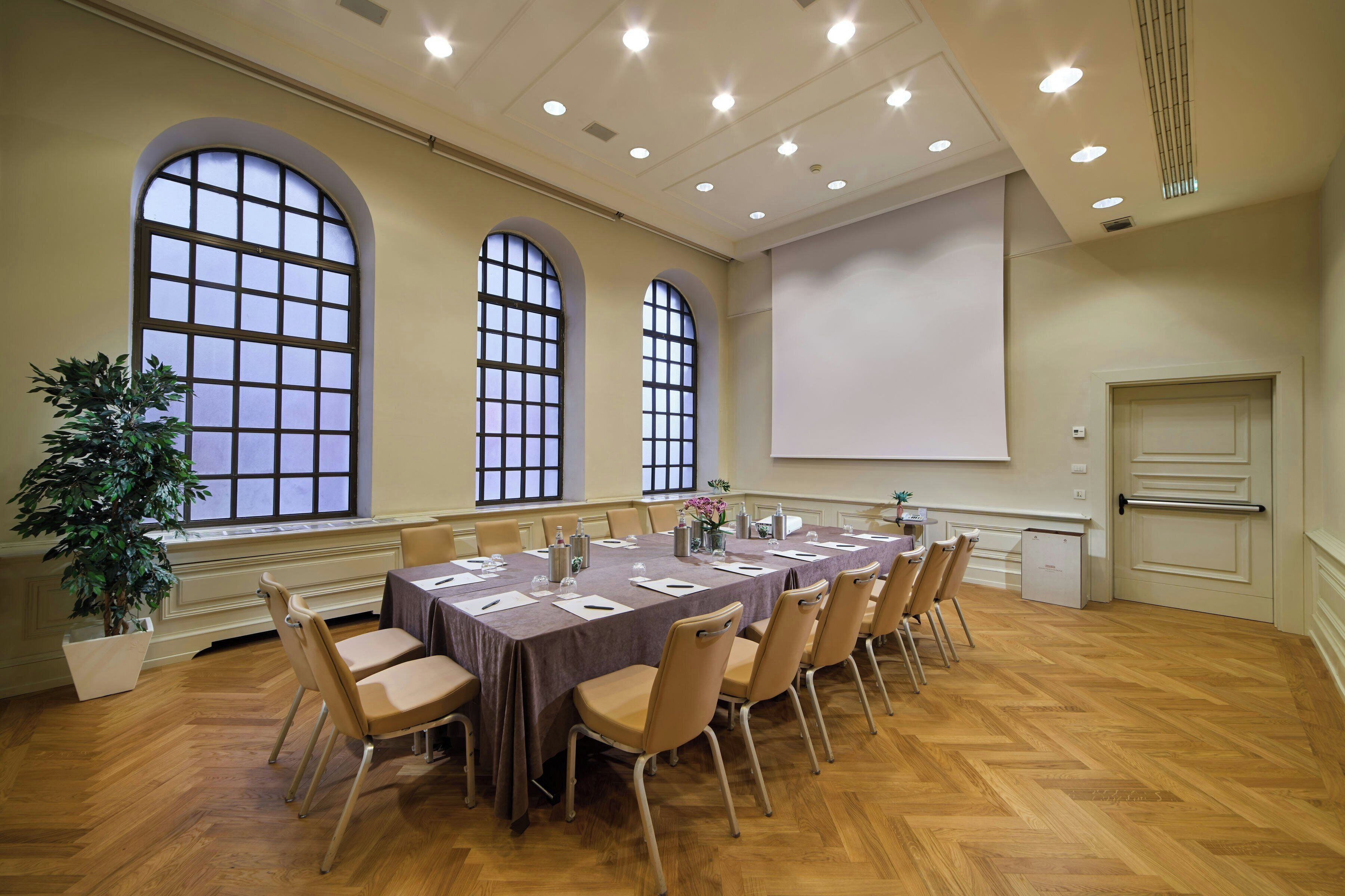 Un salón de conferencias con una larga mesa, sillas, una pantalla de proyector y un amplio ventanal.