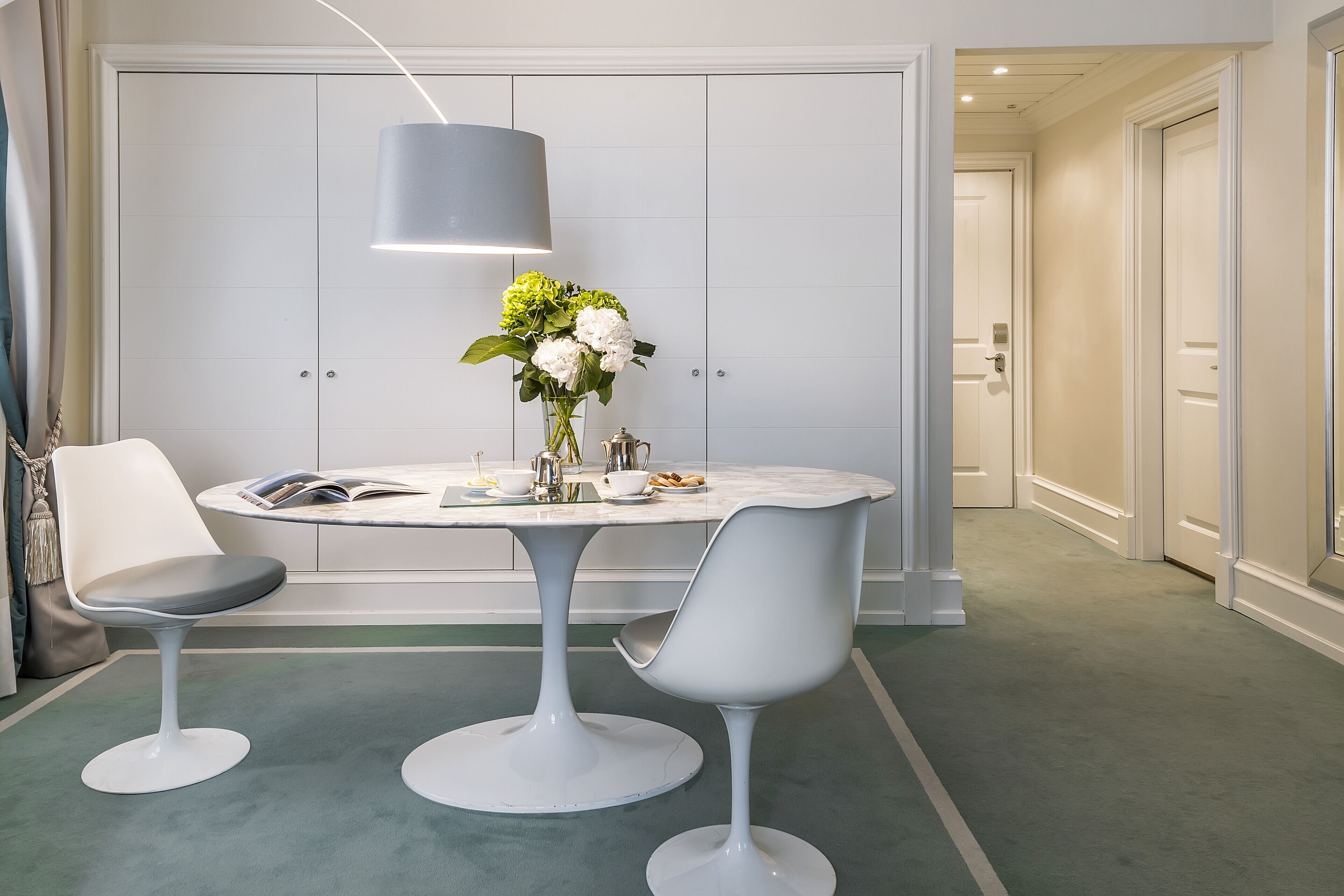 Une pièce moderne avec une table ronde, deux chaises blanches, un vase de fleurs et une lampe suspendue.