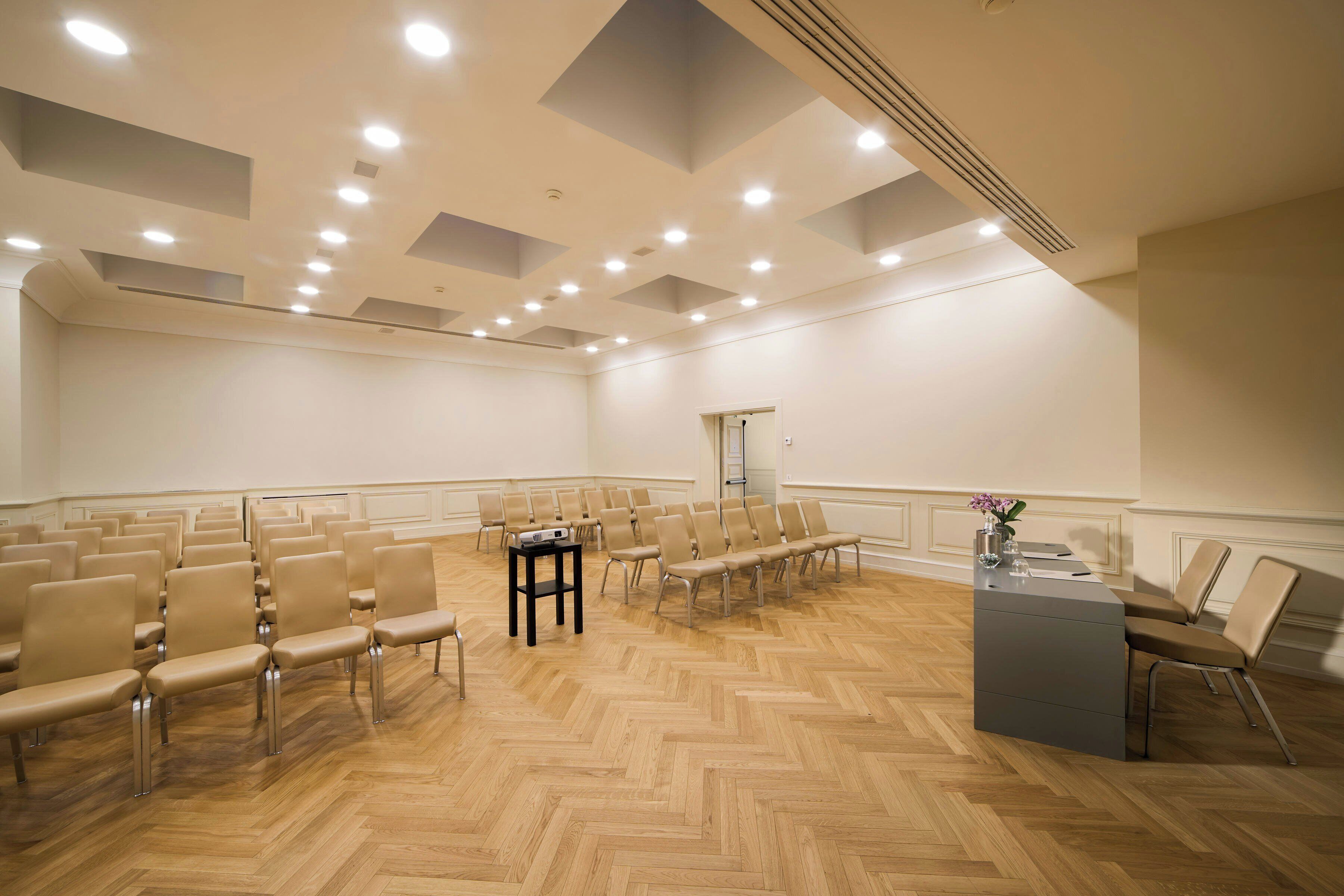 Un salón de conferencias con filas de sillas, un atril y suelo de madera.