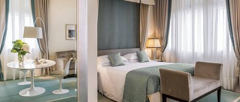 Una habitación de hotel con una cama, dos sillas, una mesa redonda con una lámpara y un espejo.
