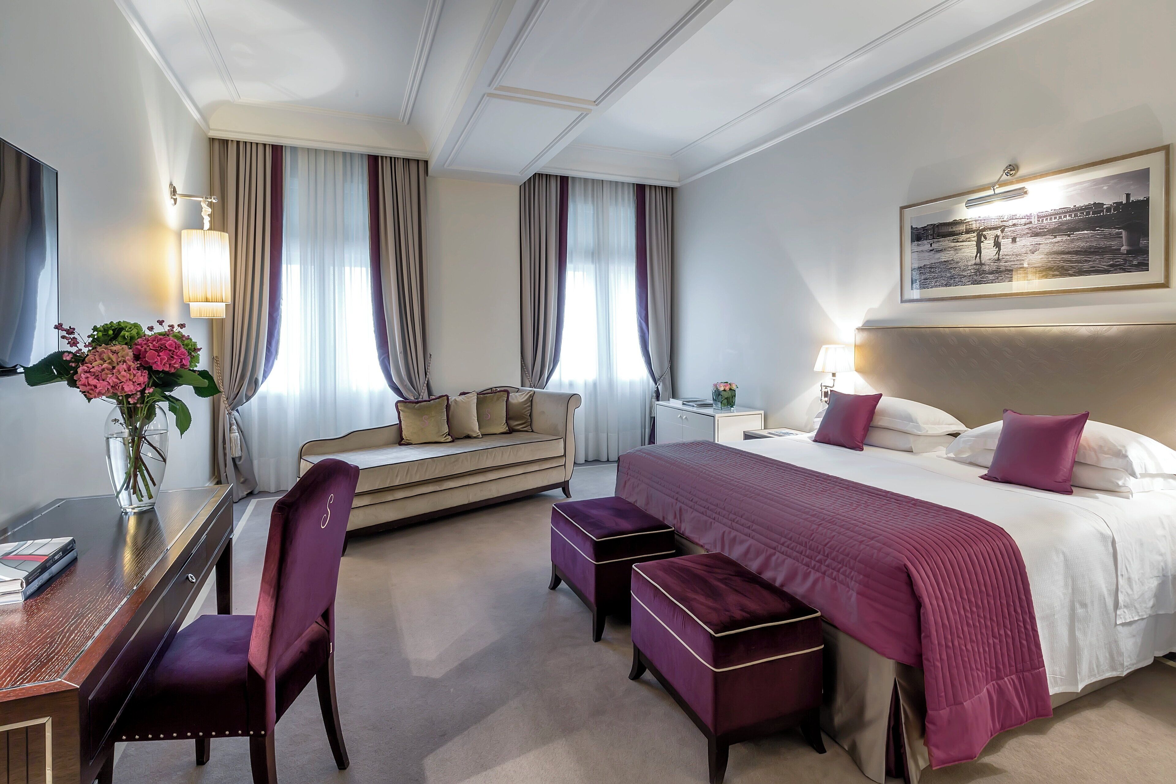 A hotel room with a large bed, a sofa, a desk, and a TV.