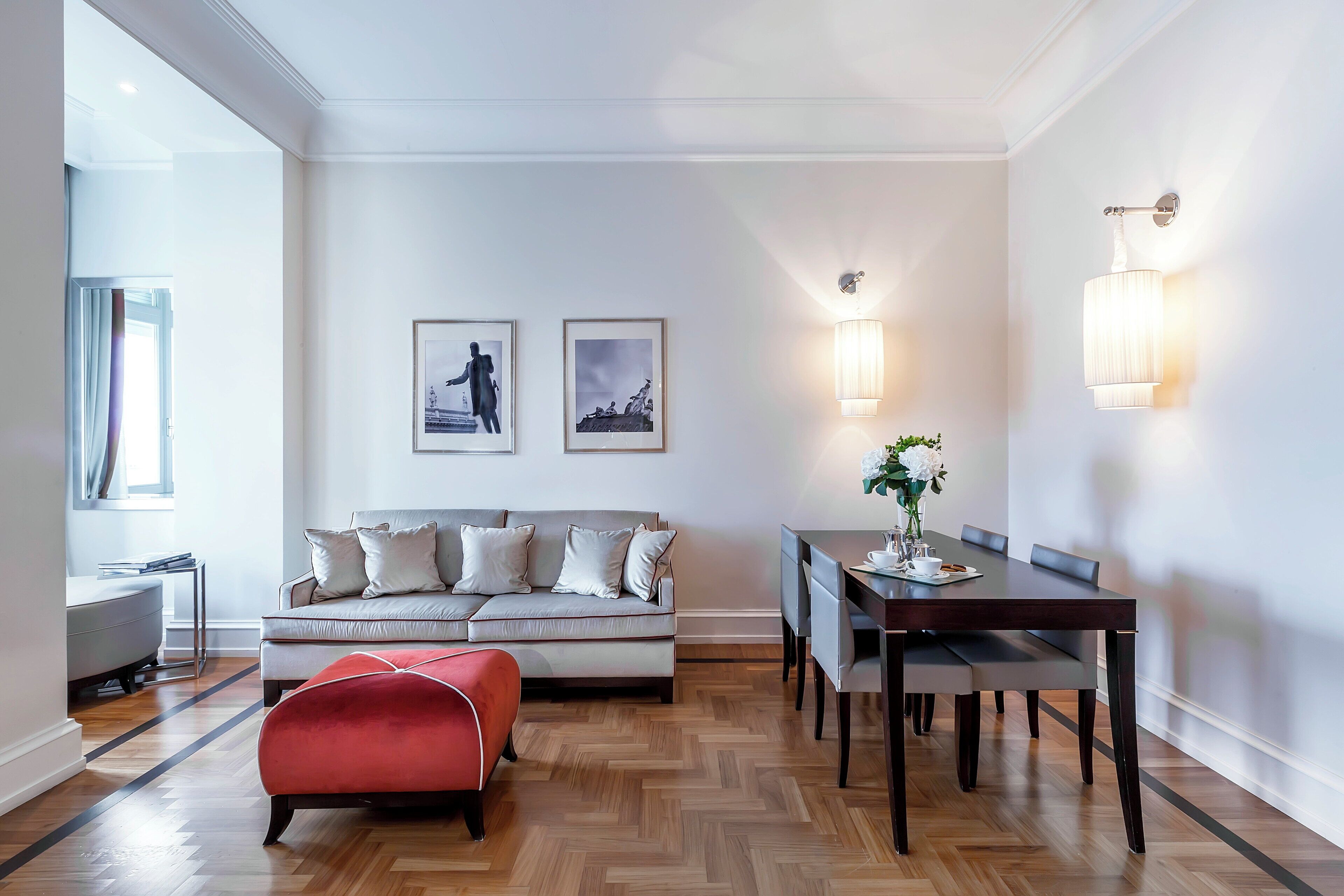 Un salon moderne comprenant un canapé, un pouf, une table à manger et des luminaires fixés au mur.