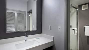 A modern bathroom with a large mirror, a white sink, and a glass-enclosed shower.