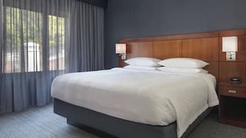 A hotel room with a large bed, dark walls, and a window with curtains.