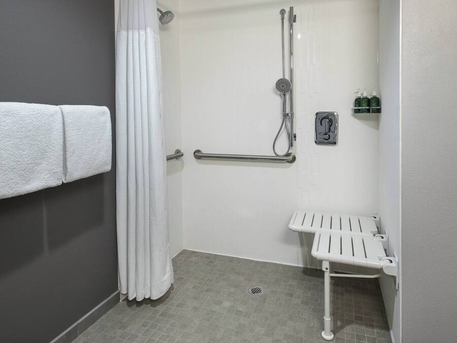 A bathroom with a shower, grab bars, a towel rack, and a small shelf with toiletries.