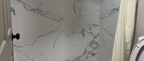 A bathroom with a shower, toilet, and marble walls.