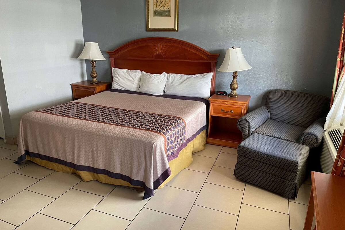Een hotelkamer met een bed, twee nachtkastjes met lampen, een stoel en een ingelijst schilderij aan de muur.