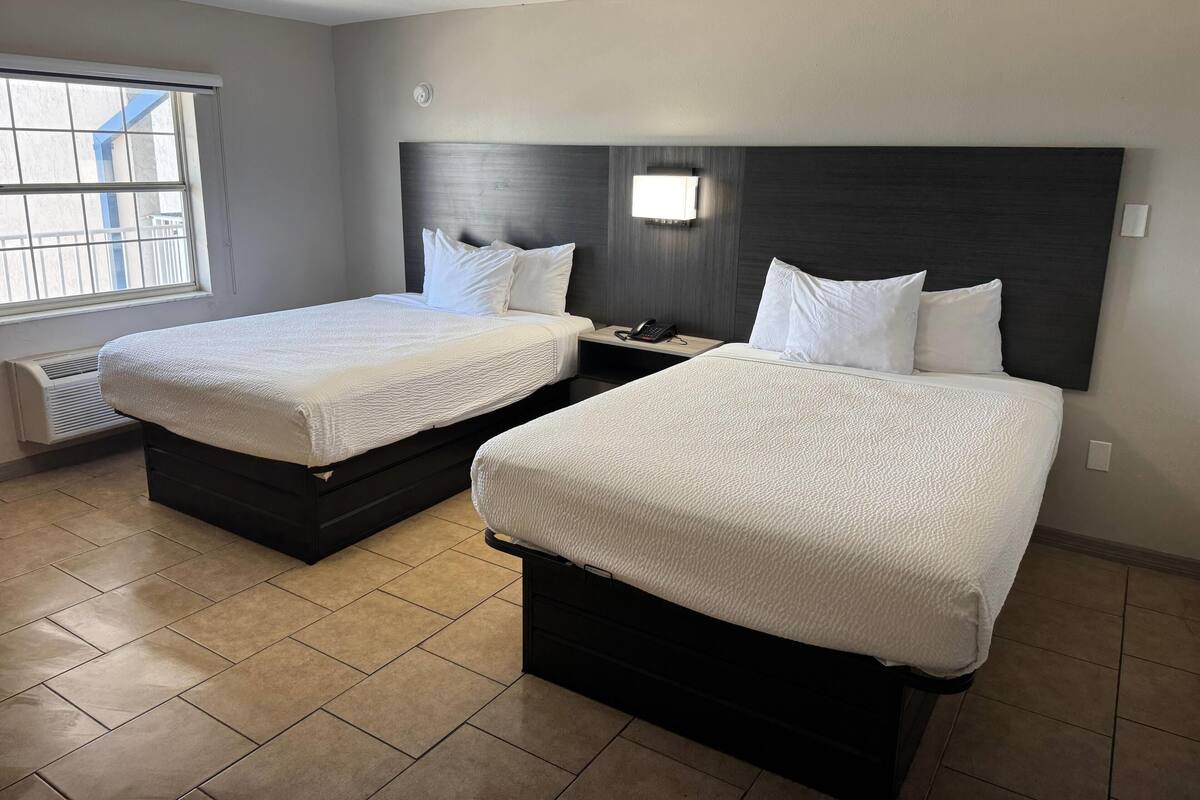 Een hotelkamer met twee bedden, een nachtkastje met een telefoon, een wandlamp en een raam met blinds.