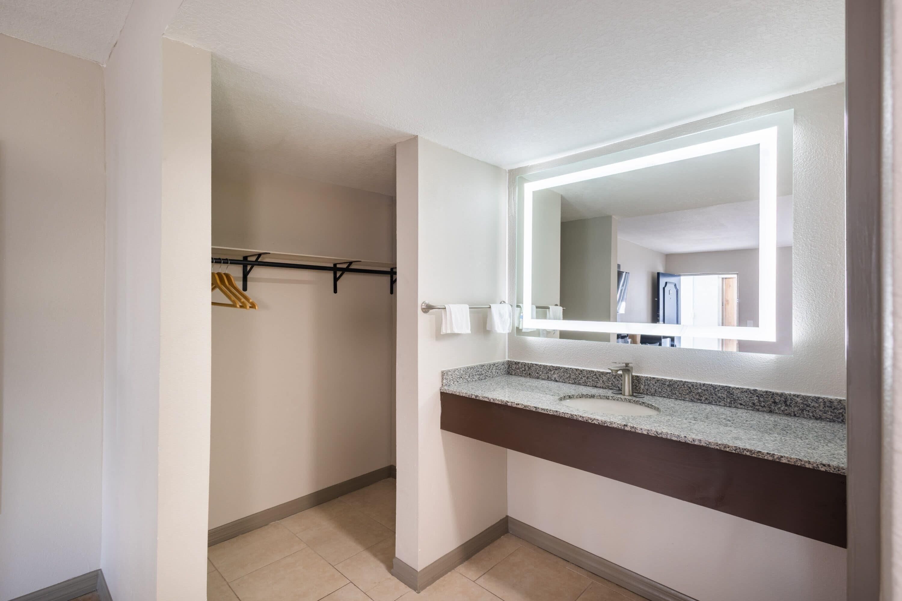 Un baño con encimera de granito, un espejo con luz y un perchero para toallas.